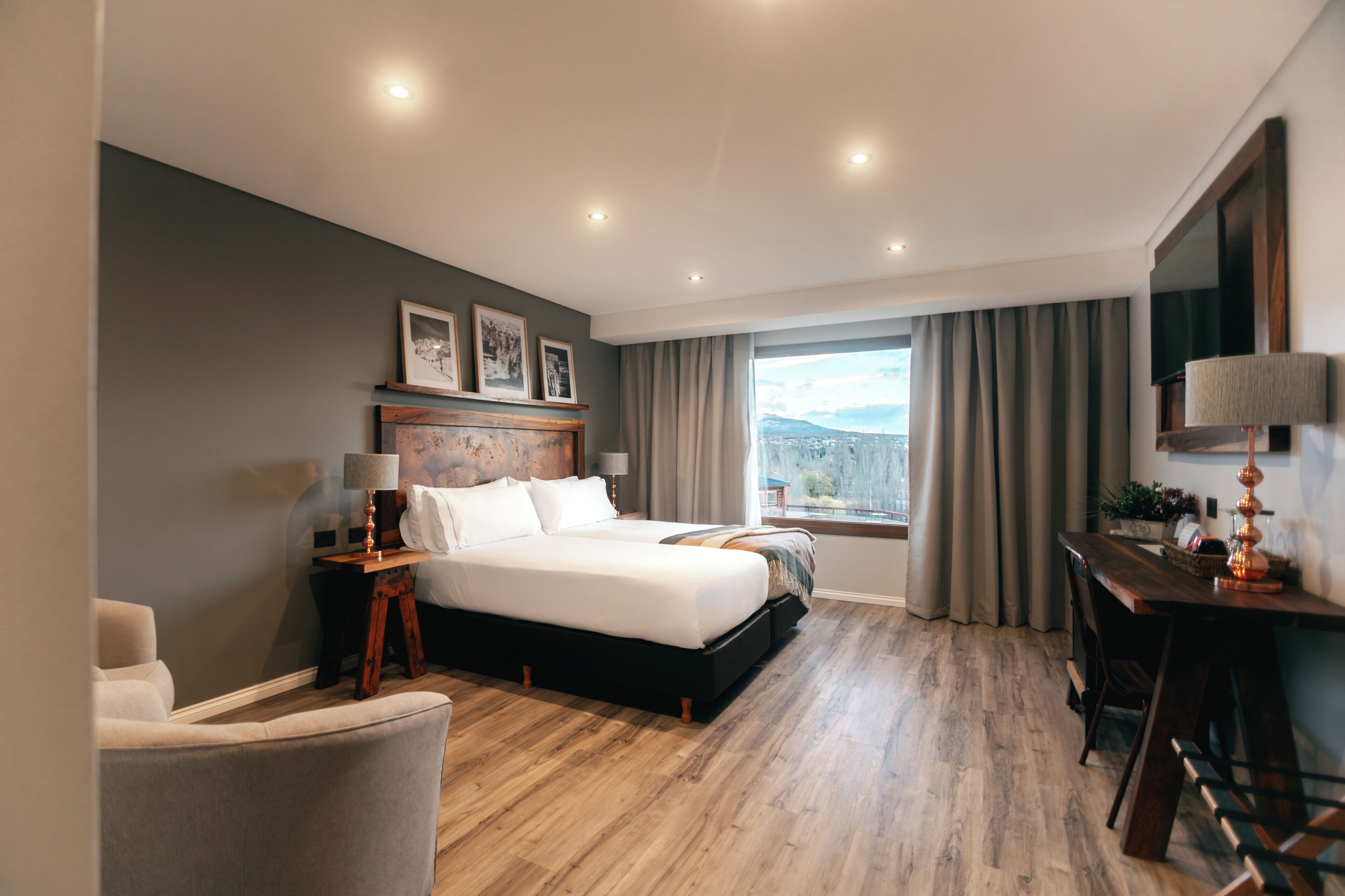 A modern hotel room with a large bed, a desk, a chair, and a view of the outdoors.