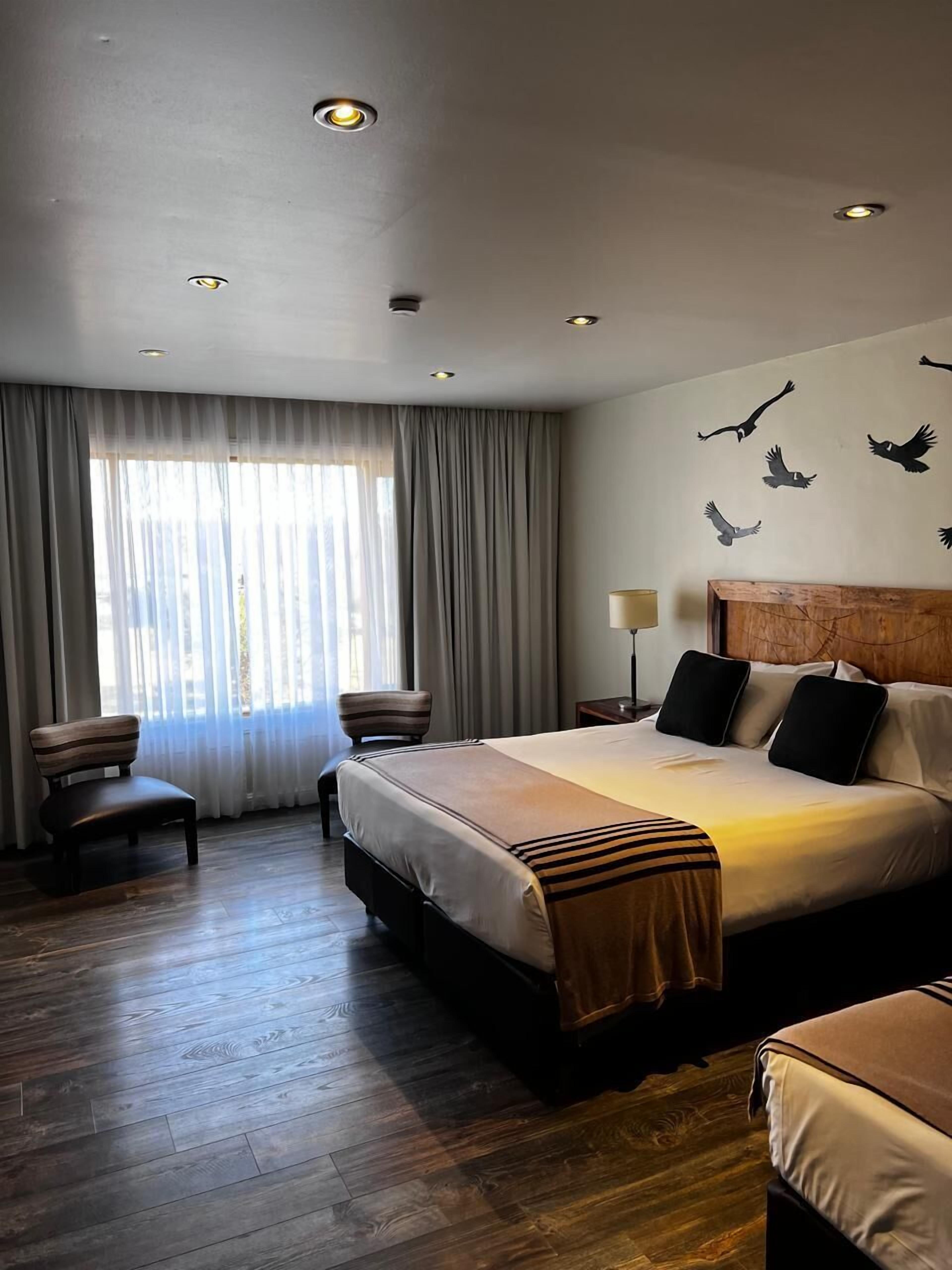 Une chambre d’hôtel avec un grand lit, un bureau, une chaise et une fenêtre avec des rideaux.