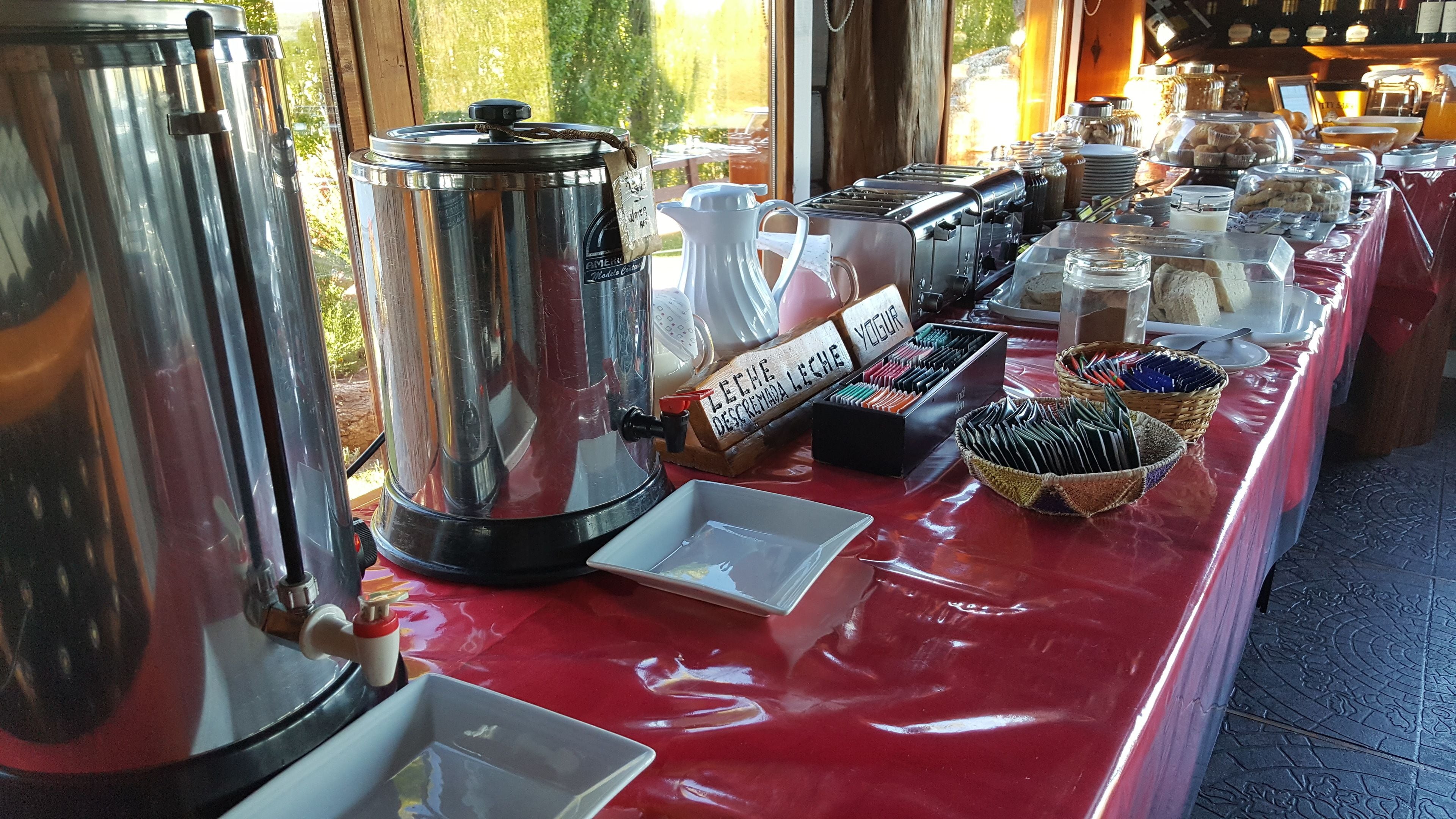 Disposição de buffet com uma estação de café, diversos recipientes de comida e toalha de mesa vermelha.