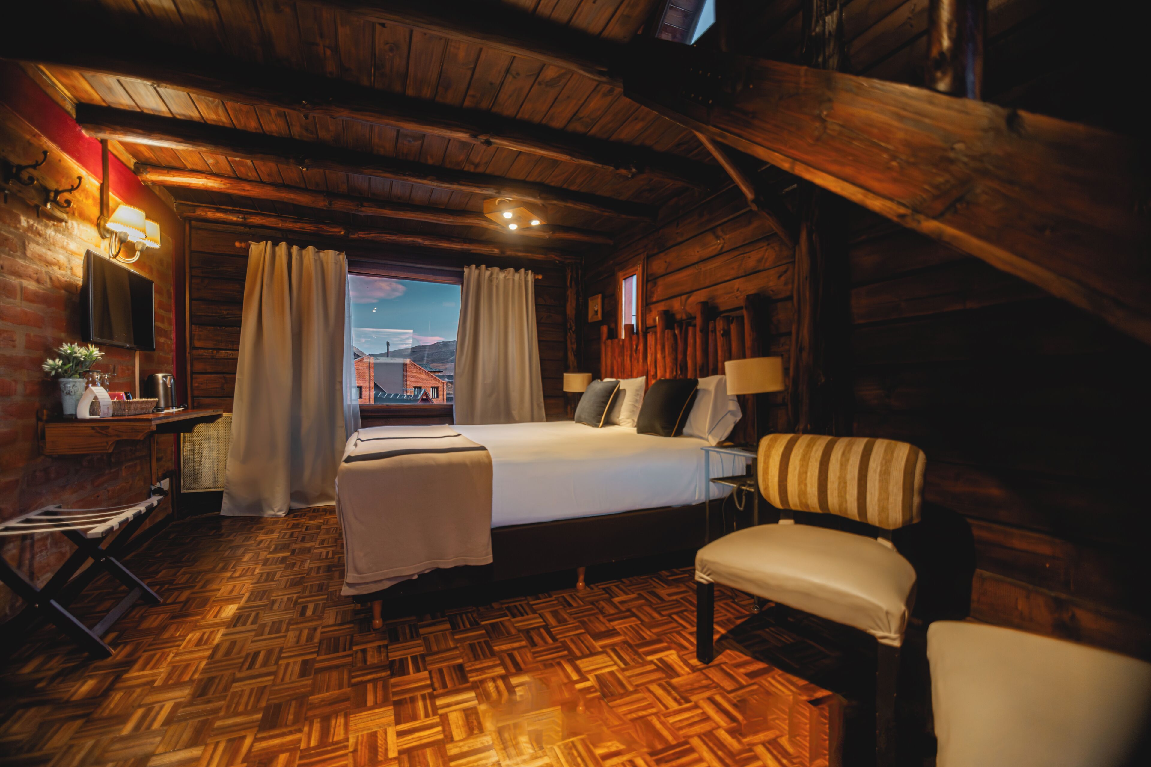 Een houten kamer in chaletstijl met een bed, een stoel, een bureau met een lamp en een televisie aan de muur.