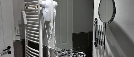 A bathroom with a white sink, a towel rack, a hairdryer, a mirror, and a shower head.
