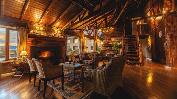 Accogliente interno di un lodge con camino, mobili in legno e una scala che conduce a un piano superiore.