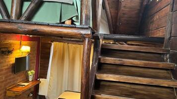 A rustic wooden staircase leading to a loft bedroom with a bed, a bedside table, and a wall-mounted TV.