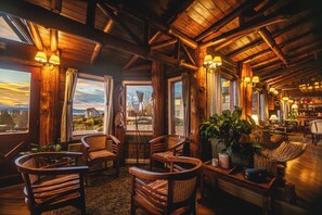 A rustic interior with wooden beams, wicker furniture, and a view of a house through a window. - Los Canelos (El Calafate)