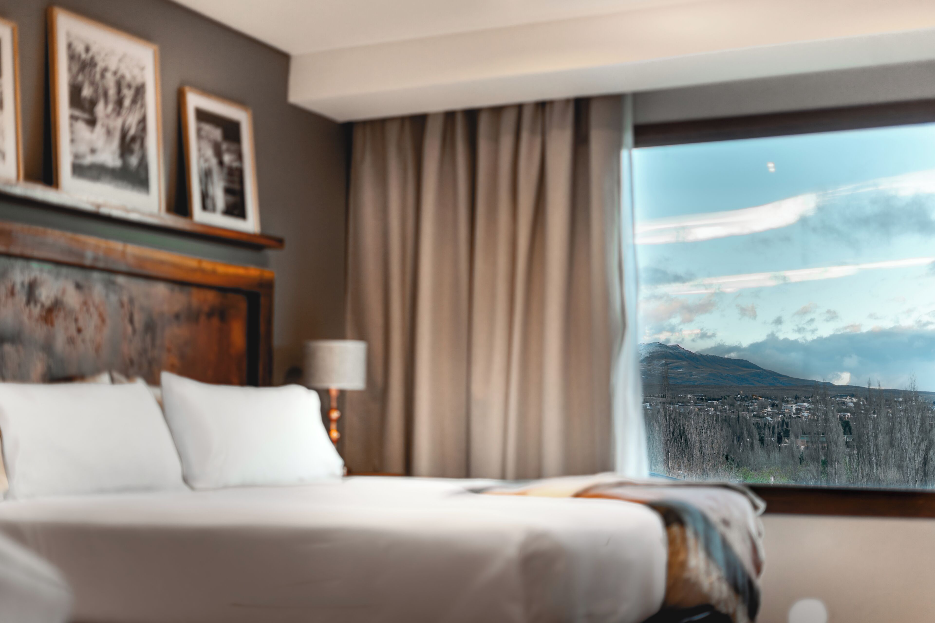 Habitación de hotel con cama, lámpara, cuadros en la pared y ventana con vistas a la montaña.