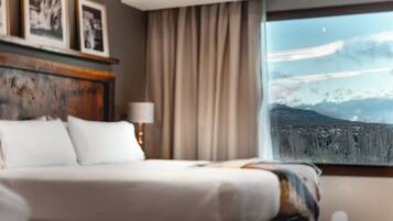 Habitación de hotel con cama, lámpara, cuadros en la pared y ventana con vistas a la montaña.
