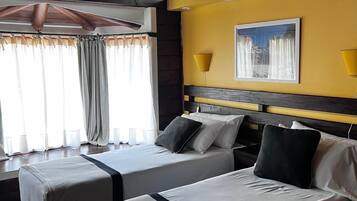 A room with two beds, wooden beams on the ceiling, a yellow wall, and a window with curtains.