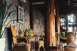 A room with wicker furniture, a stone wall, and a large wooden pillar. - Los Canelos (El Calafate)