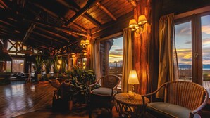 Un interno in legno con mobili in vimini, un tavolo con una candela e vista attraverso ampie finestre.