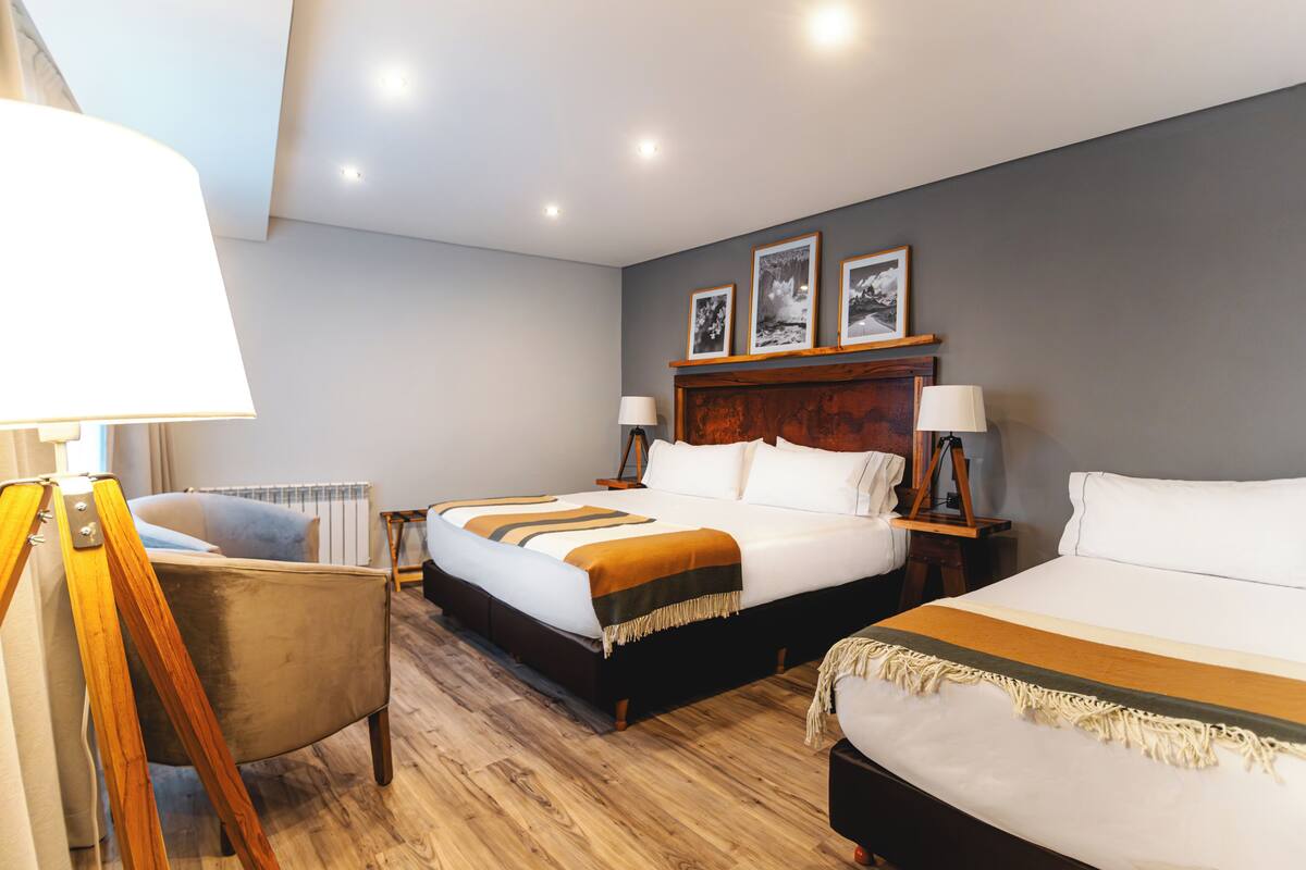 A hotel room with two beds, a wooden floor, a radiator, and a lamp.