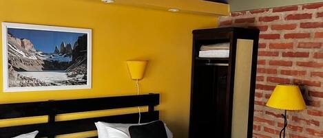 Habitación de hotel con dos camas, una pared amarilla, una pared de ladrillo y un cuadro enmarcado en la pared.