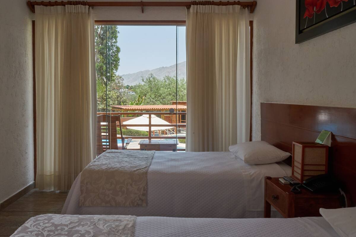 Ein Hotelzimmer mit Bett, Nachttisch und Blick auf einen Außenbereich mit Tisch und Stühlen.