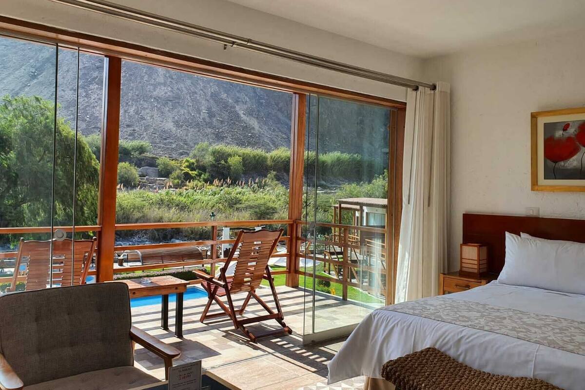 Ein Hotelzimmer mit großem Fenster und Blick auf die Berge, einem Bett, einem Holztisch und einem Stuhl.