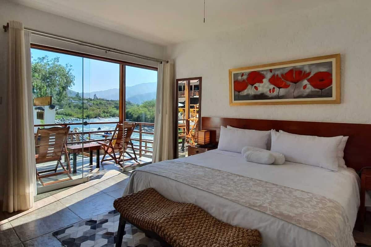 Ein geräumiges Schlafzimmer mit einem großen Bett, Blick auf einen Fluss und einem Balkon mit Tisch und Stühlen.