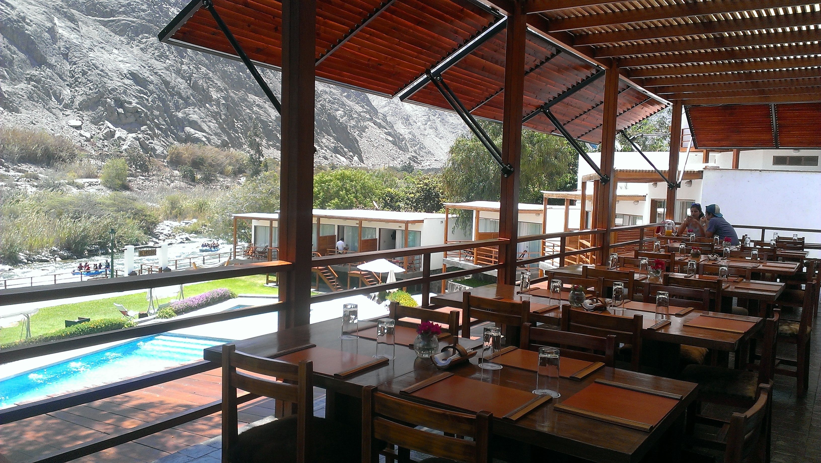 Un restaurante con terraza al aire libre, con vistas a una piscina y un paisaje montañoso.