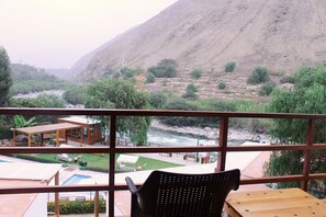 A terrace with a view of a river, a wooden deck, and a pool area.