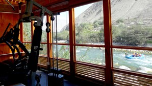Une salle de sport équipée de matériel d’exercice et dotée de grandes fenêtres donnant sur une rivière et des montagnes.