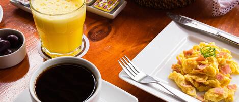 A breakfast table with a plate of scrambled eggs, a glass of orange juice, a cup of coffee, and a basket of bread.