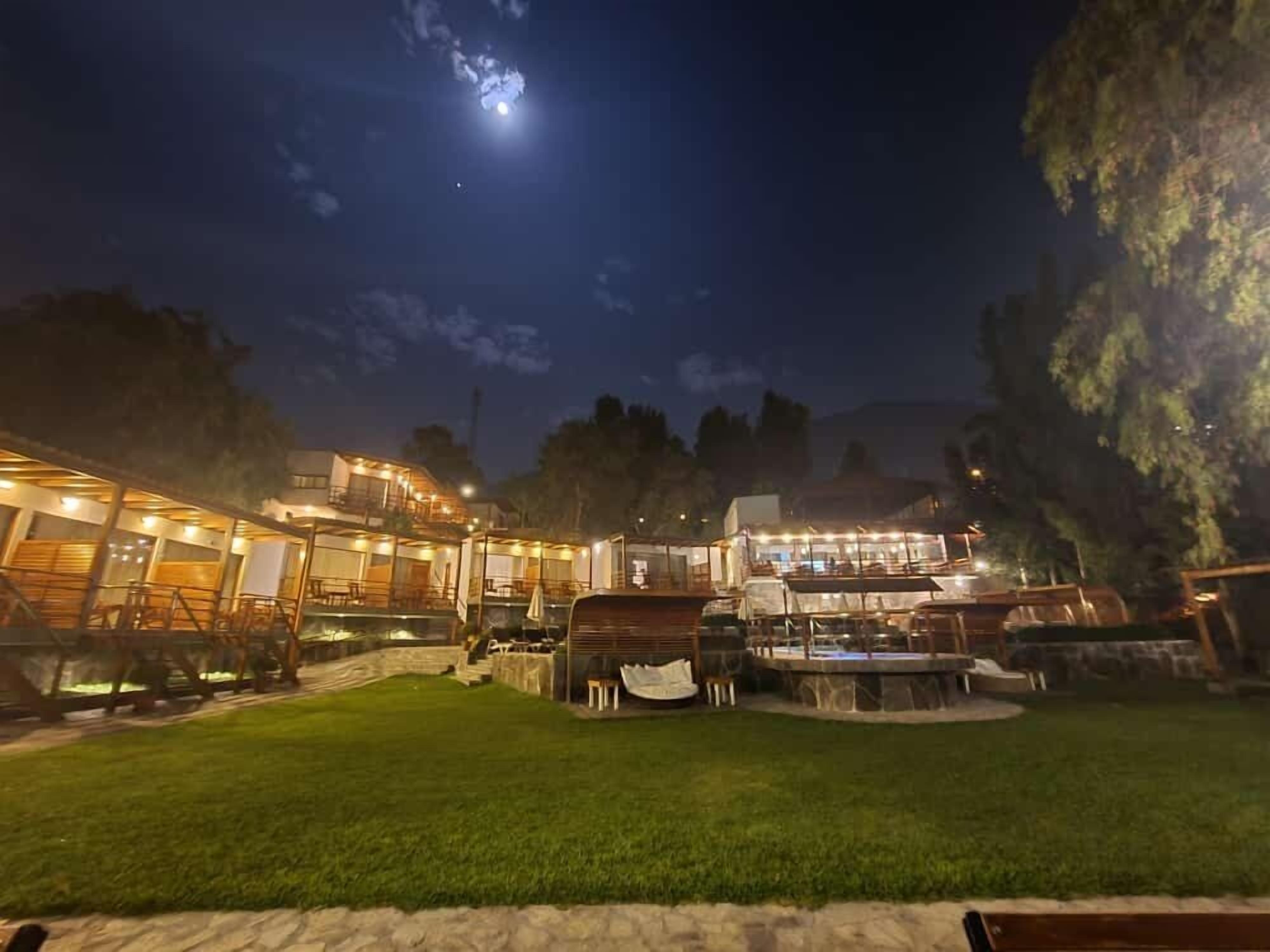 Un espacio exterior bien iluminado con varios edificios, un césped y un árbol grande.