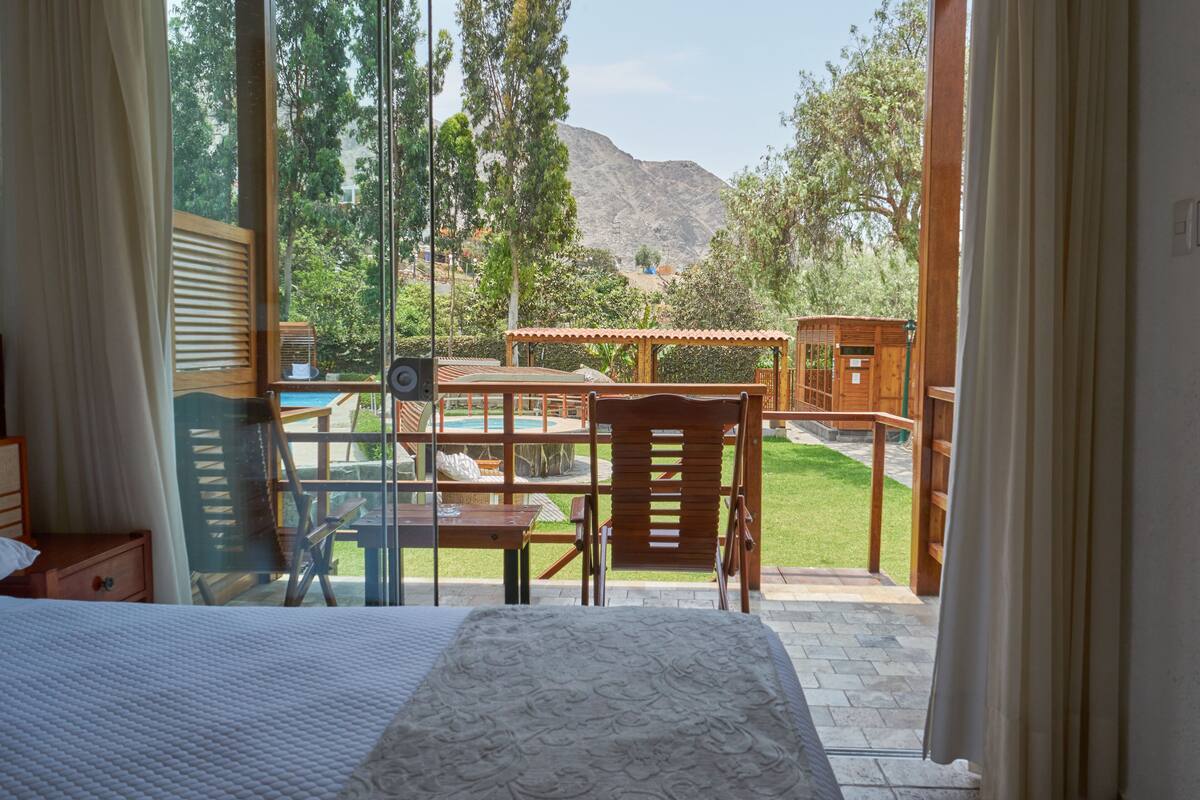 Ein Schlafzimmer mit einem großen Bett, einem Holzstuhl, einem Tisch und Blick auf einen Pool und Berge.
