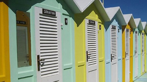 A row of colorful beach huts with shutters, each labeled with a name and number. - Hotel Alba (Misano Adriatico)