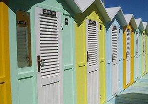 A row of colorful beach huts with shutters, each labeled with a name and number. - Hotel Alba (Misano Adriatico)