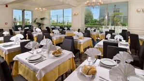 A banquet hall with multiple tables set for dining, featuring white tablecloths and yellow sashes. - Hotel Alba (Misano Adriatico)