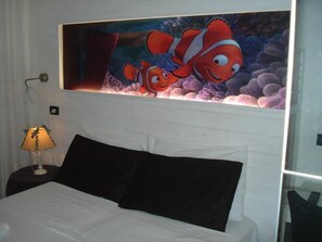 A hotel room with a bed, a nightstand with a lamp, and a large painting of two clownfish on the wall. - Hotel Alba (Misano Adriatico)