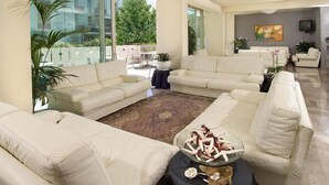 A spacious living room with a large L-shaped sofa set, a glass coffee table, and a view of the outdoors through large windows. - Hotel Alba (Misano Adriatico)
