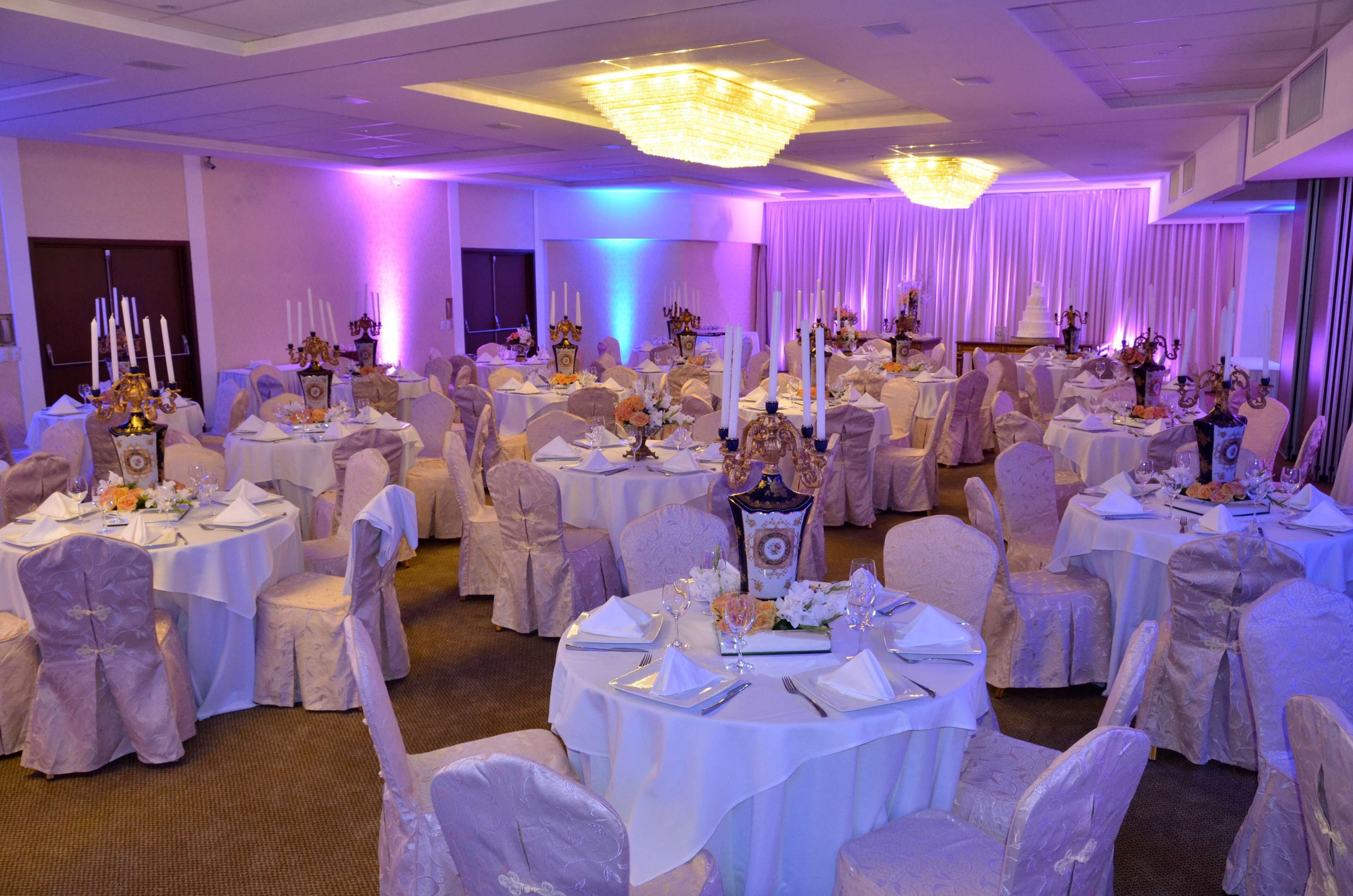 A banquet hall with round tables, white tablecloths, and chairs covered in white fabric.