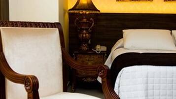 A bedroom with a wooden chair, a bedside table with a lamp, and a bed with white bedding.
