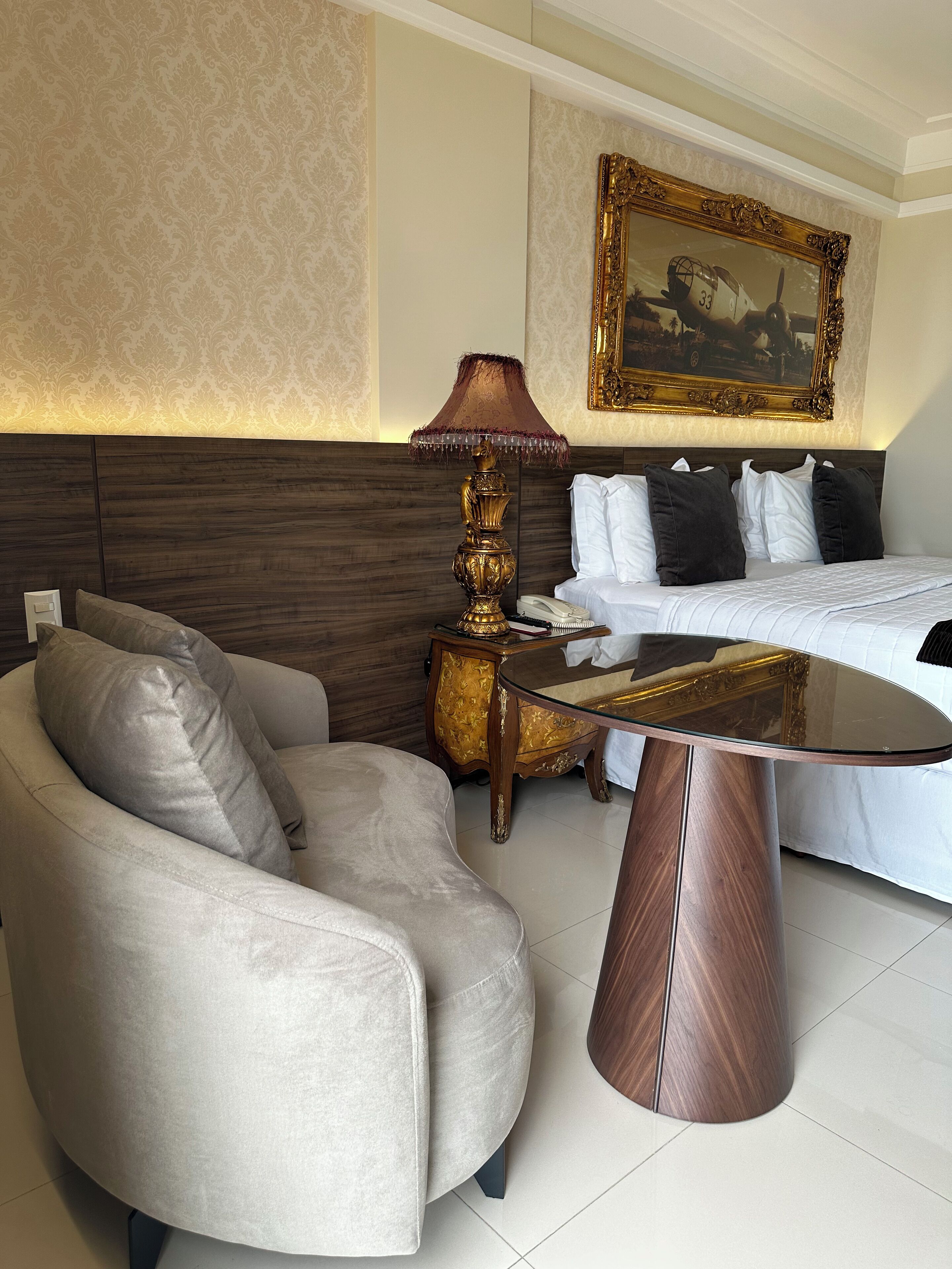 A hotel room with a bed, a sofa, a lamp, and a painting on the wall.