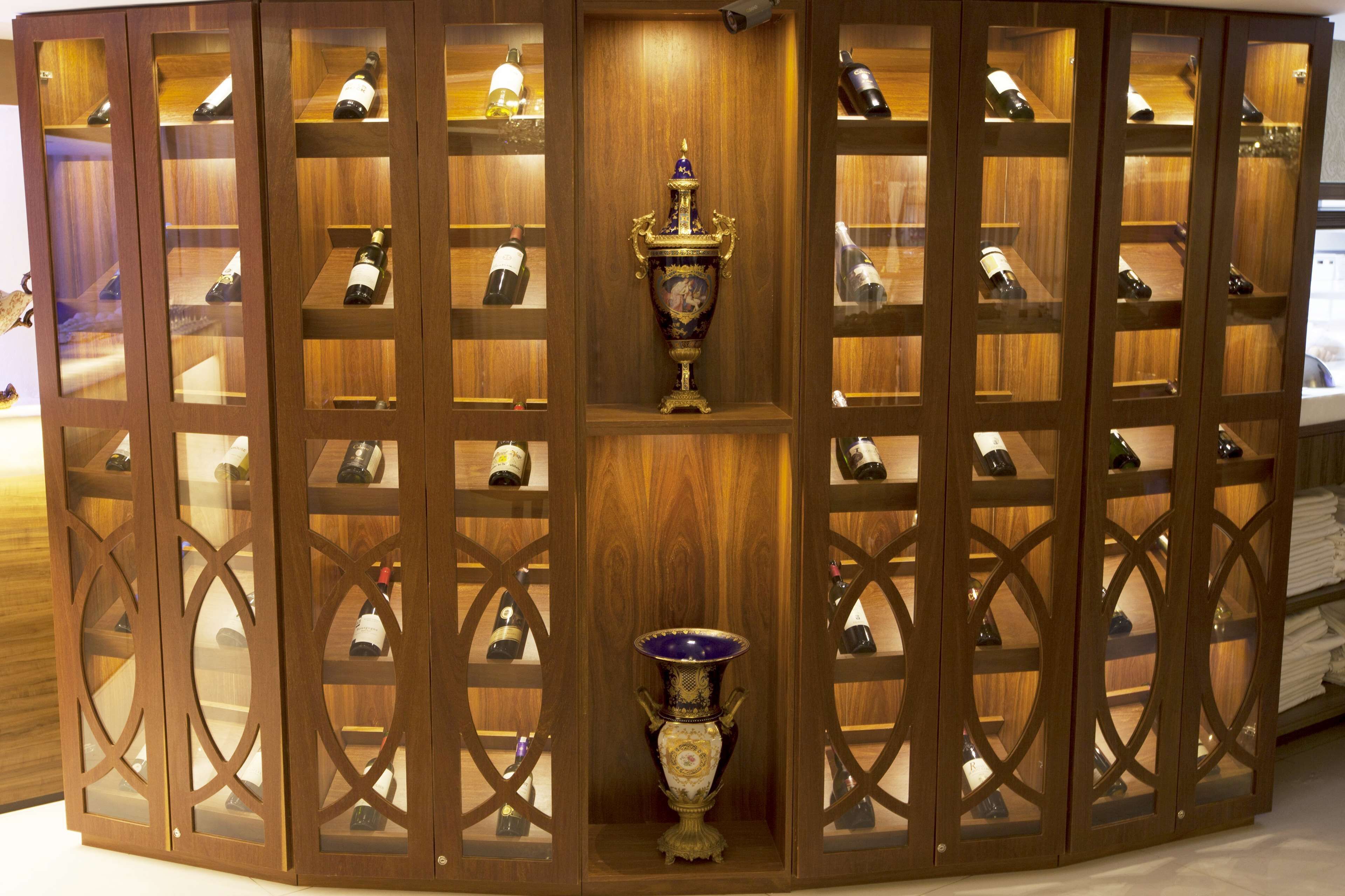 A wooden display cabinet with multiple shelves containing bottles, a central ornate vase, and a patterned design.