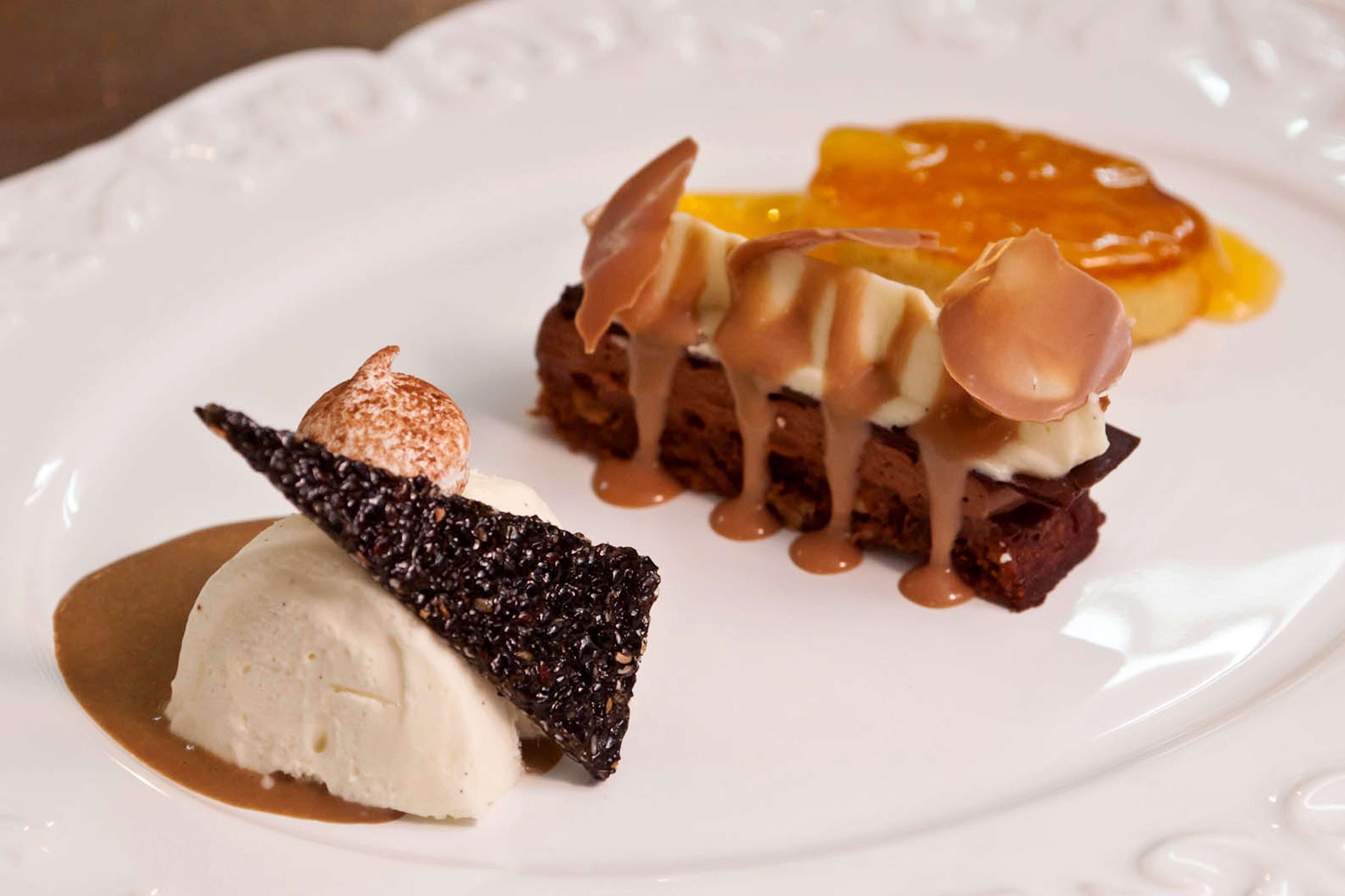 A dessert plate with a scoop of vanilla ice cream, a chocolate-covered biscuit, and a caramel drizzle.