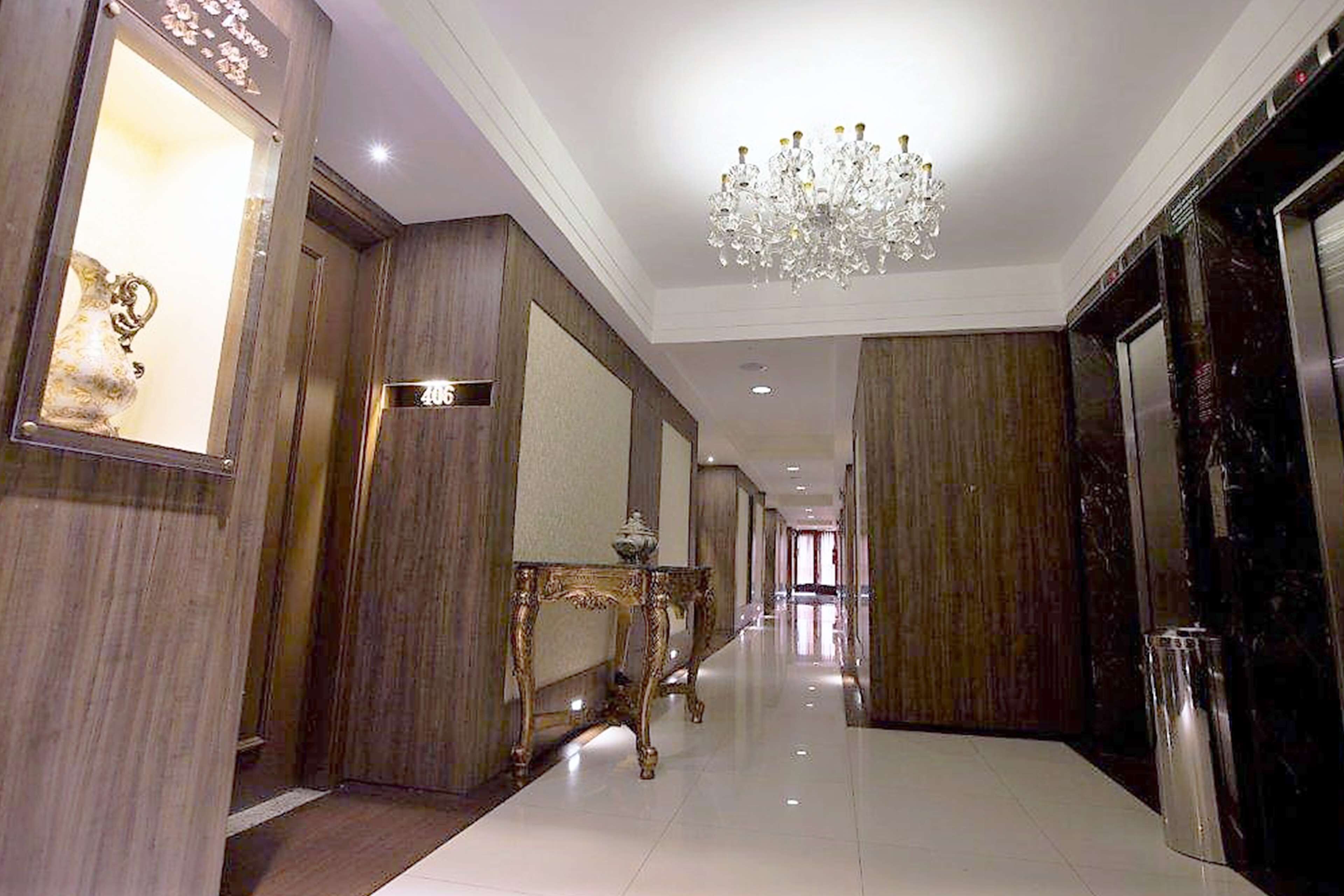 Um corredor com um candelabro, um espelho e uma porta.