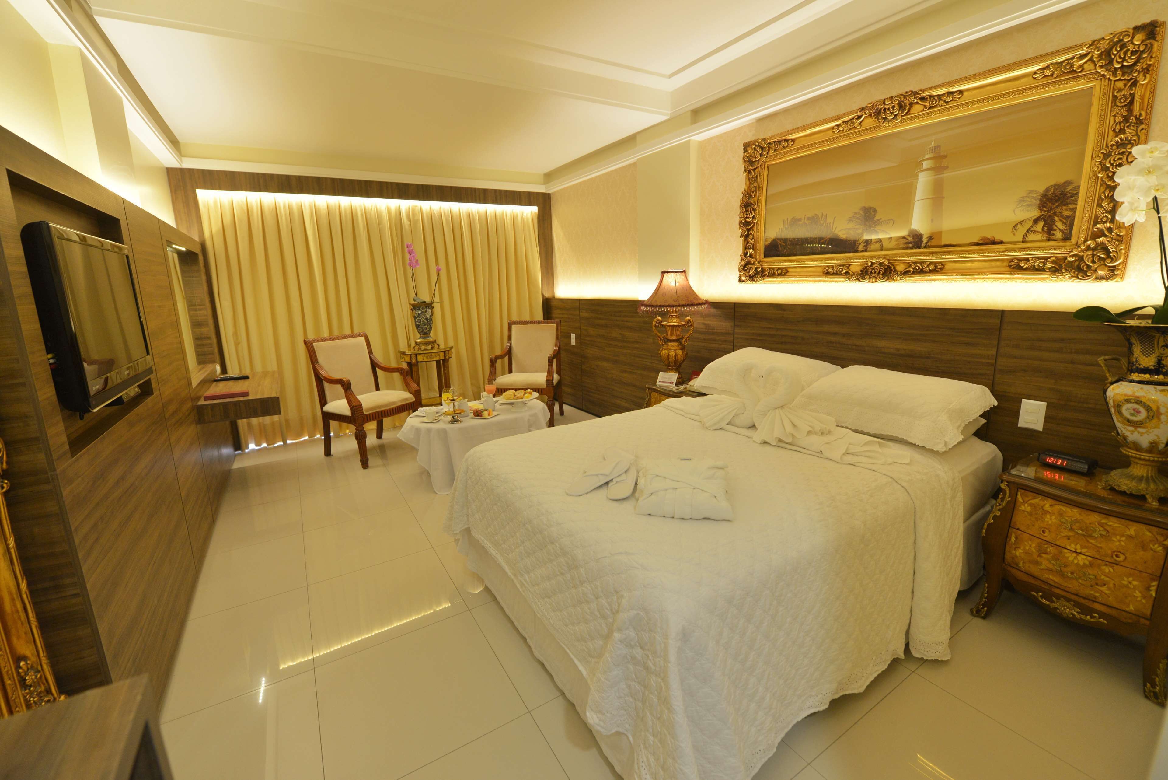 A hotel room with a large bed, two chairs, a small table, a TV, and a decorative mirror.