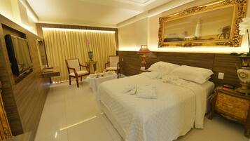 Habitación de hotel con una cama grande, dos sillones, una mesita, un televisor y un espejo decorativo.