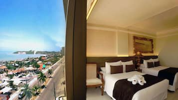 Quarto de hotel com duas camas, vista da cidade e da costa, um quadro na parede e um abajur.