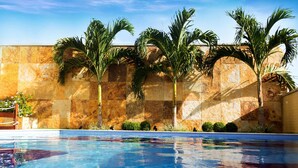 Ein Swimmingpool mit klarem, blauem Wasser, umgeben von Palmen und einer Steinmauer.