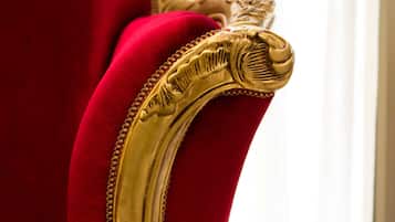 A close-up of a red velvet chair with gold ornate detailing.