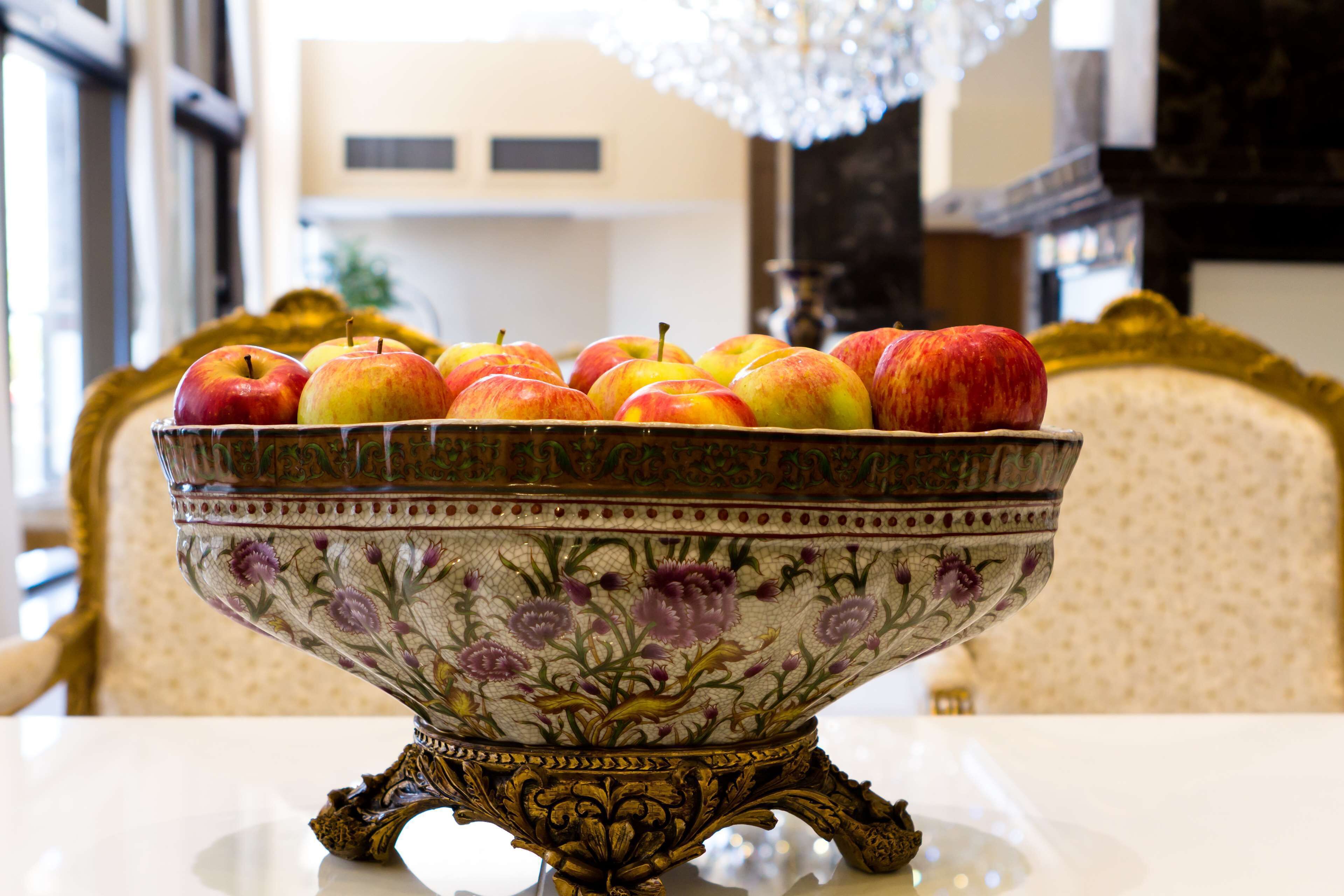 Un tazón decorativo con estampado floral que contiene manzanas sobre una mesa.