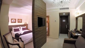 Camera d'hotel con un letto, una TV a parete, una poltrona, un divano e un lampadario.
