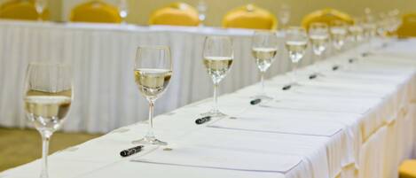 Una larga mesa con varios vasos de vino alineados, cubierta con un mantel blanco, y sillas amarillas al fondo.