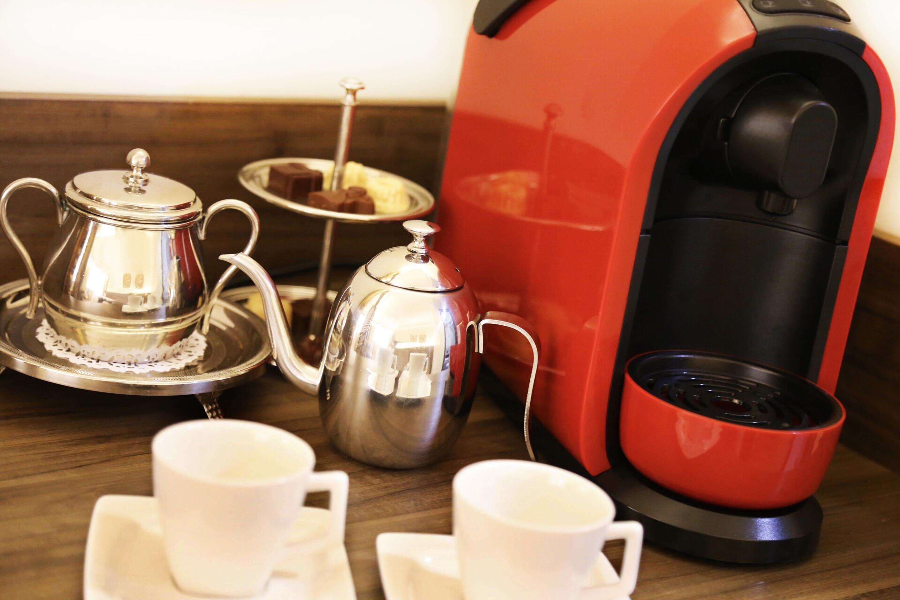 A coffee maker, a silver teapot, and two white cups on a wooden table.