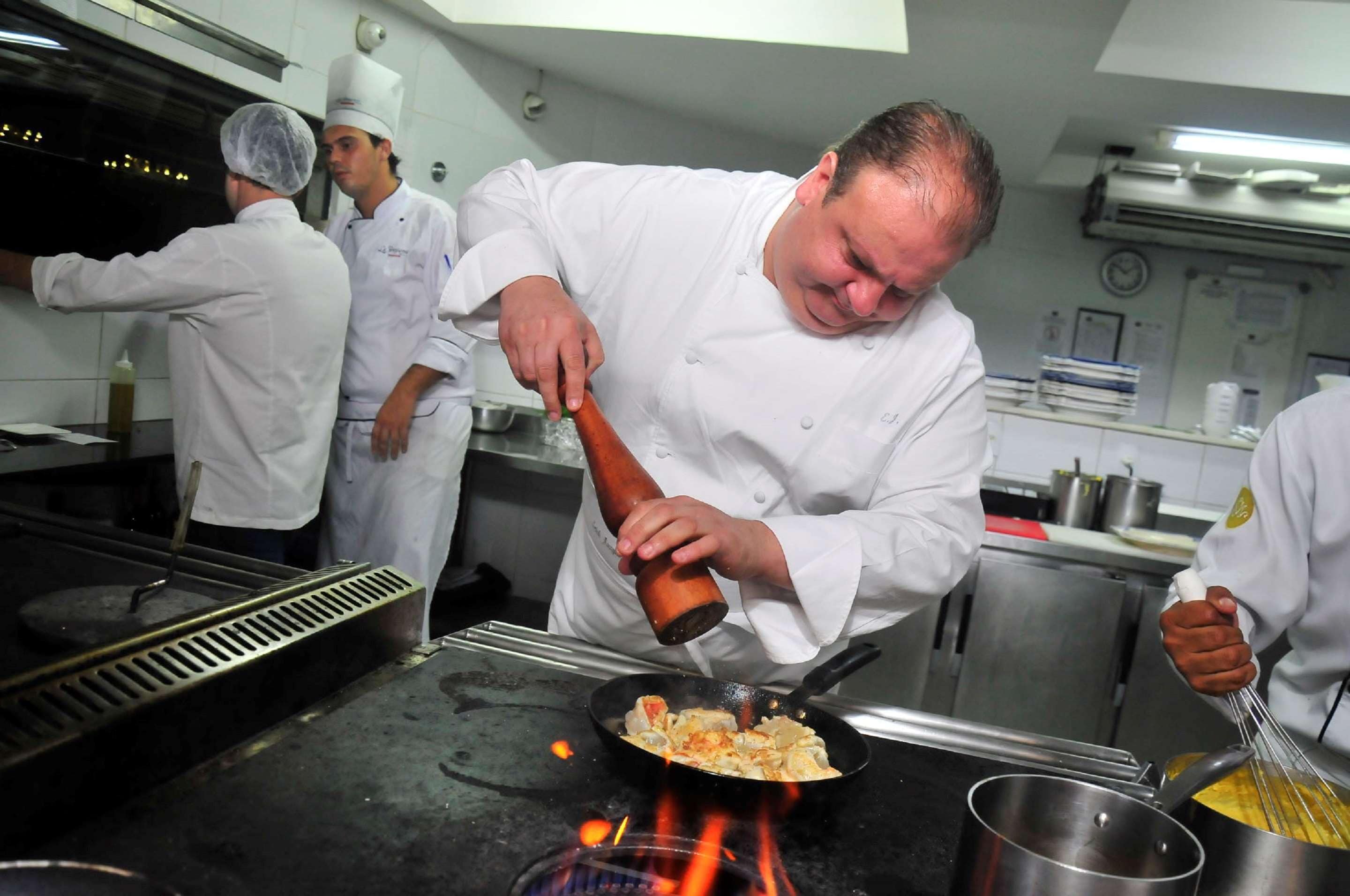 A chef in a professional kitchen, preparing food on a stove.
