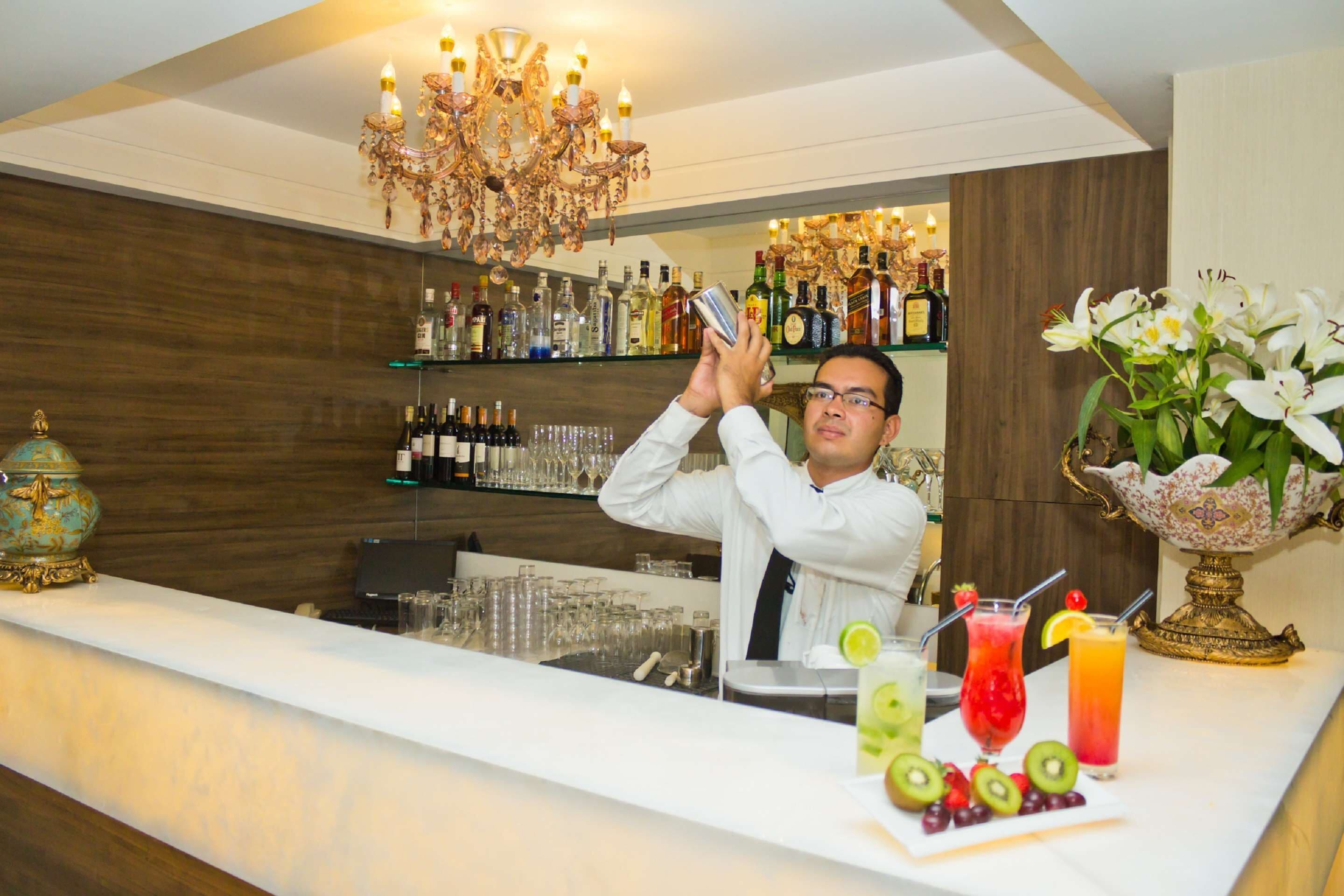A bar area with a bartender, a chandelier, and a variety of liquor bottles and glasses.