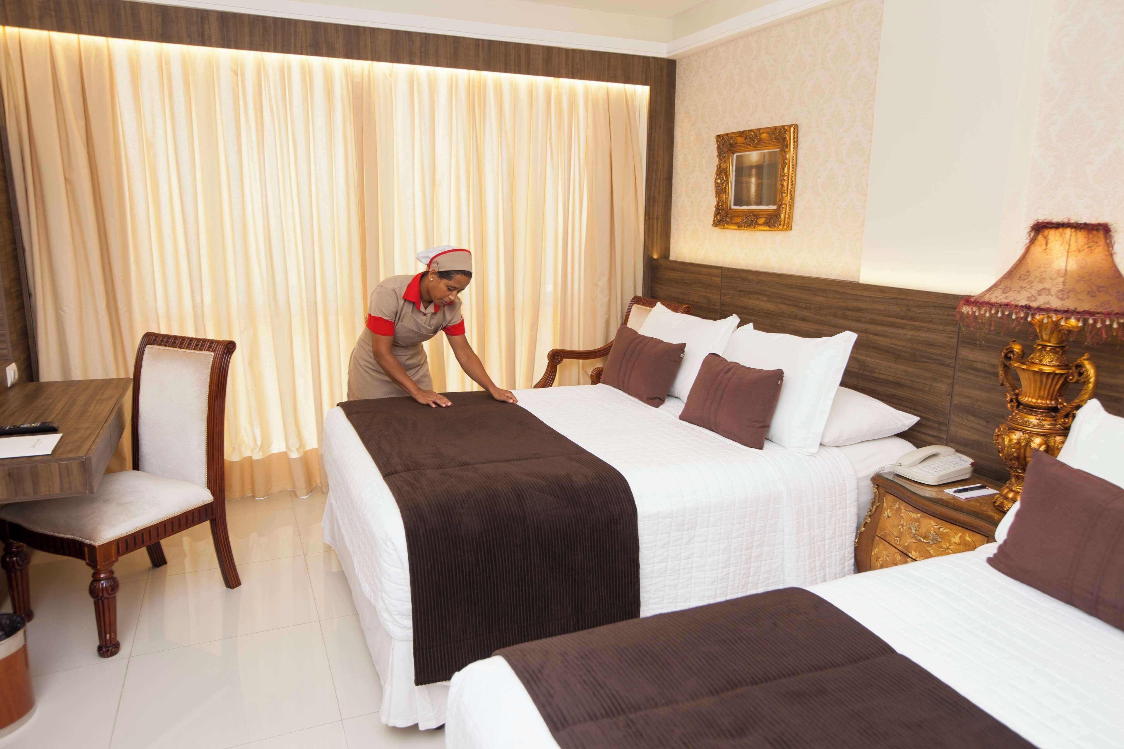 A hotel room with two beds, a desk, a chair, a nightstand with a lamp, and a curtain.