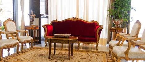 A luxurious room with a red velvet sofa, ornate chairs, a patterned rug, and a large potted plant.