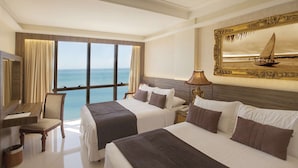 Ein Hotelzimmer mit zwei Betten, einem Schreibtisch, einem Sessel und einem großen Fenster mit Blick aufs Meer.
