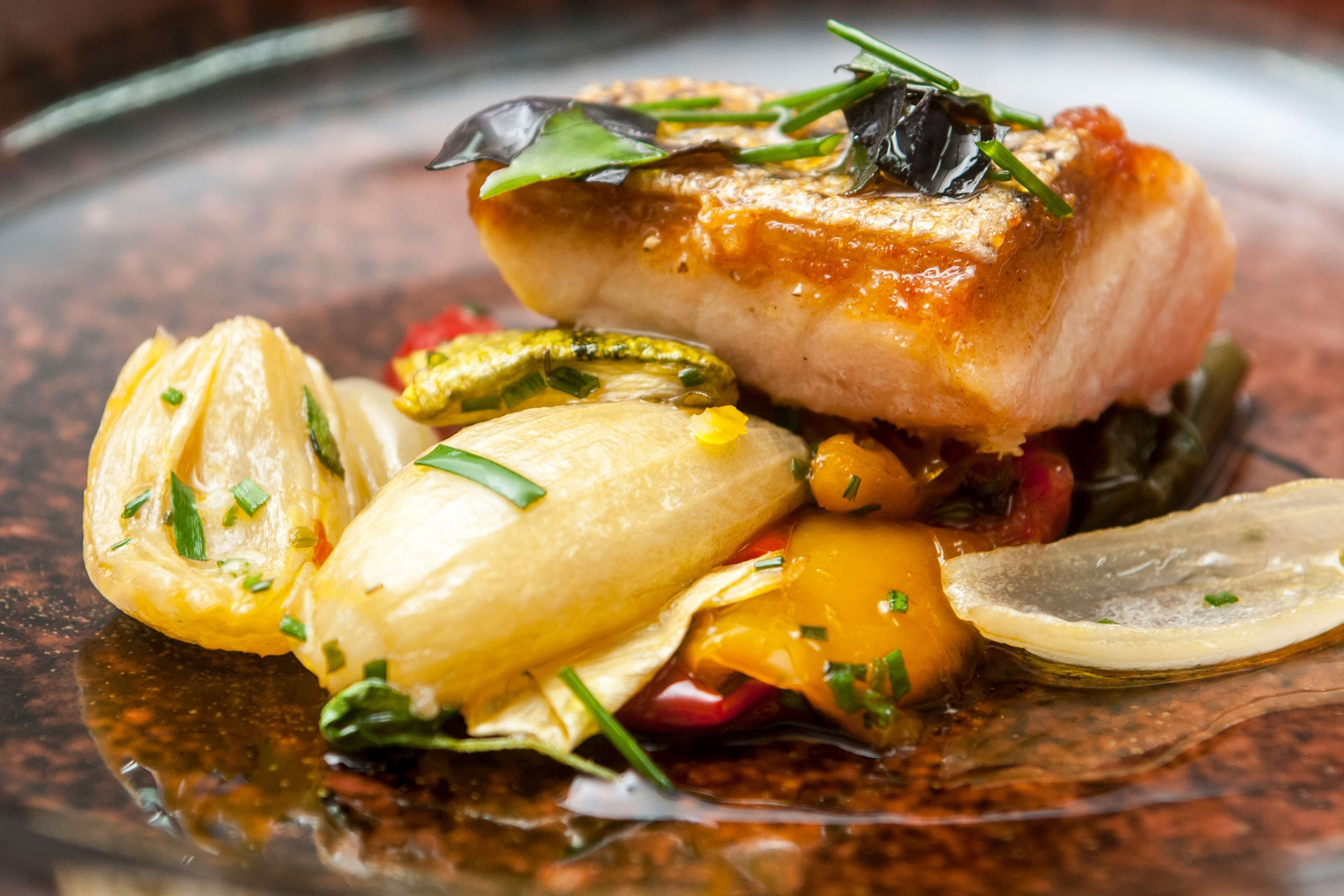 Un plat composé d’un morceau de poisson, de légumes et d’une sauce, le tout présenté dans une assiette.